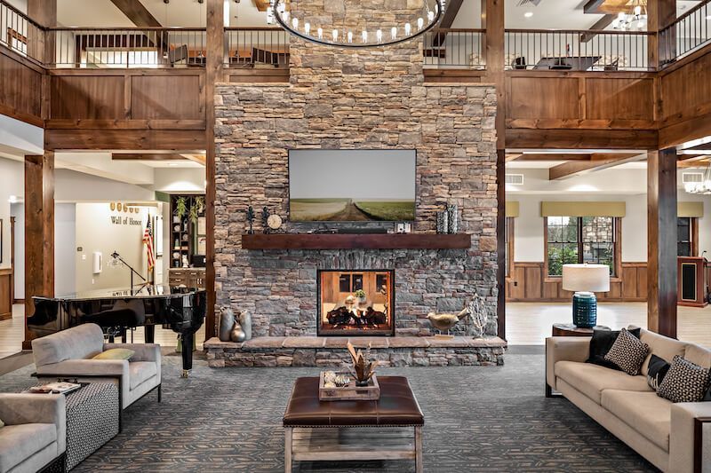 Lobby with stone fireplace, TV, and wood accents. Sofas, piano, and chandelier create a cozy atmosphere.