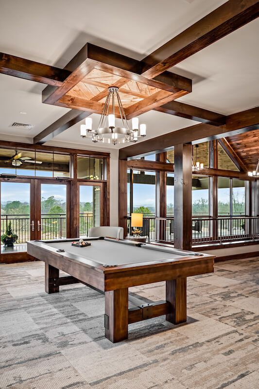 Pool table in a room with exposed wooden beams, large windows, and a chandelier.
