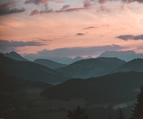 A sunset over a mountain range with a pink sky