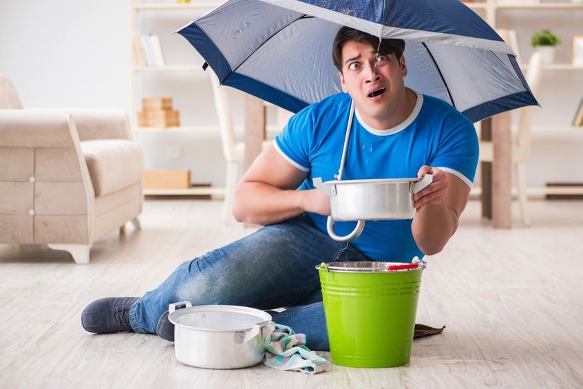 A man is sitting on the floor with an umbrella over his head.