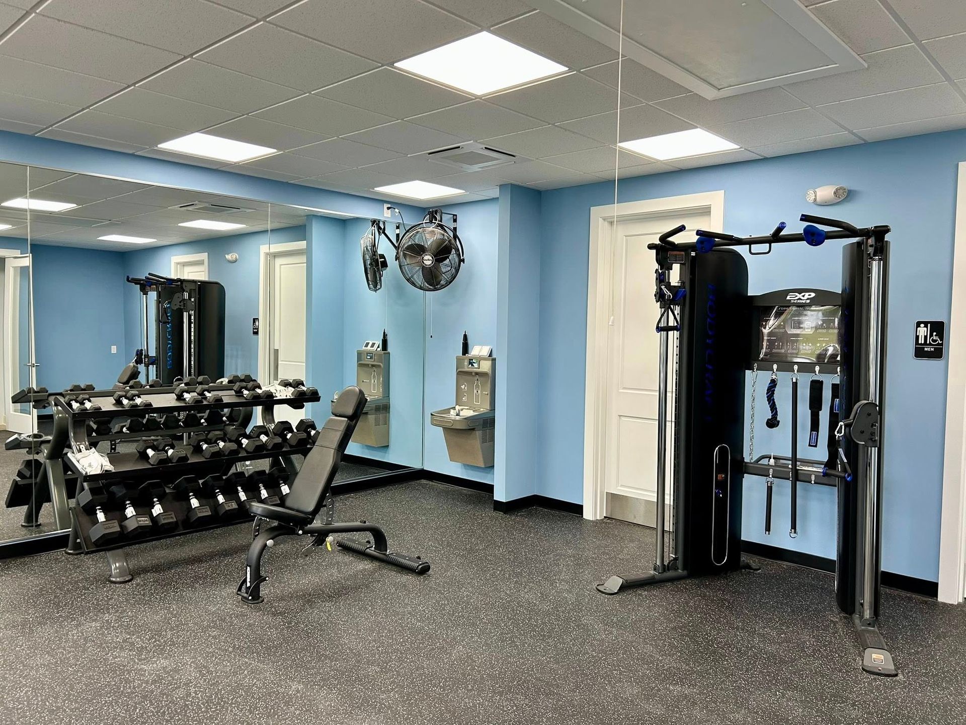 A gym with blue walls , a bench , dumbbells , and a mirror.