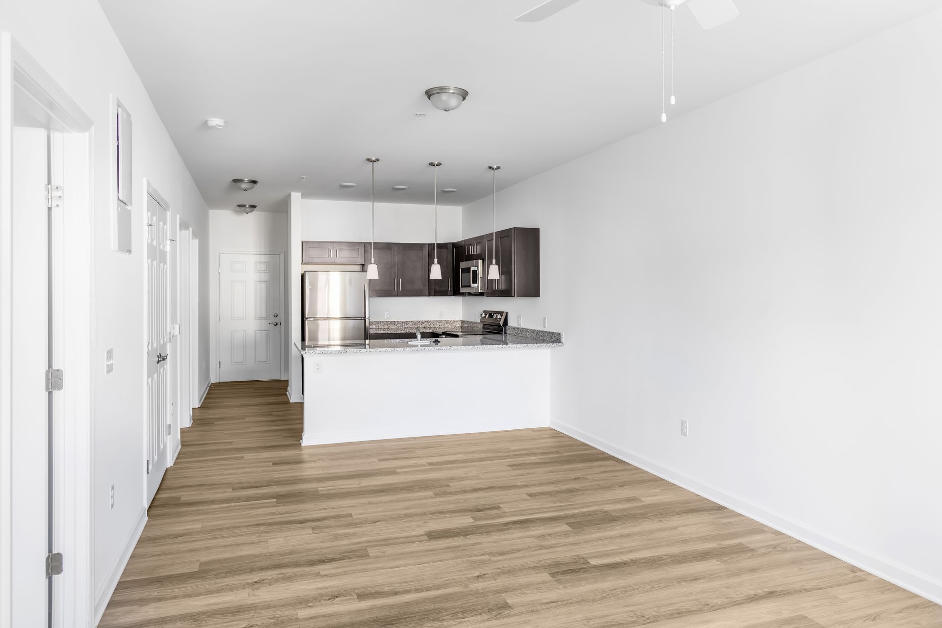 Empty apartment interior with kitchen, stainless steel appliances, and wood floors.