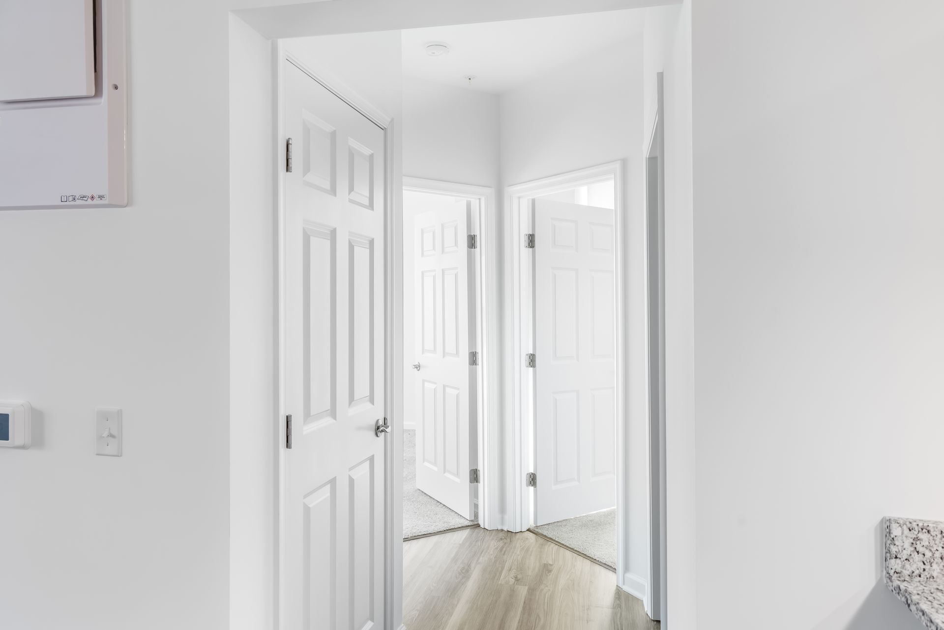 White hallway with three closed doors; light wood floor.