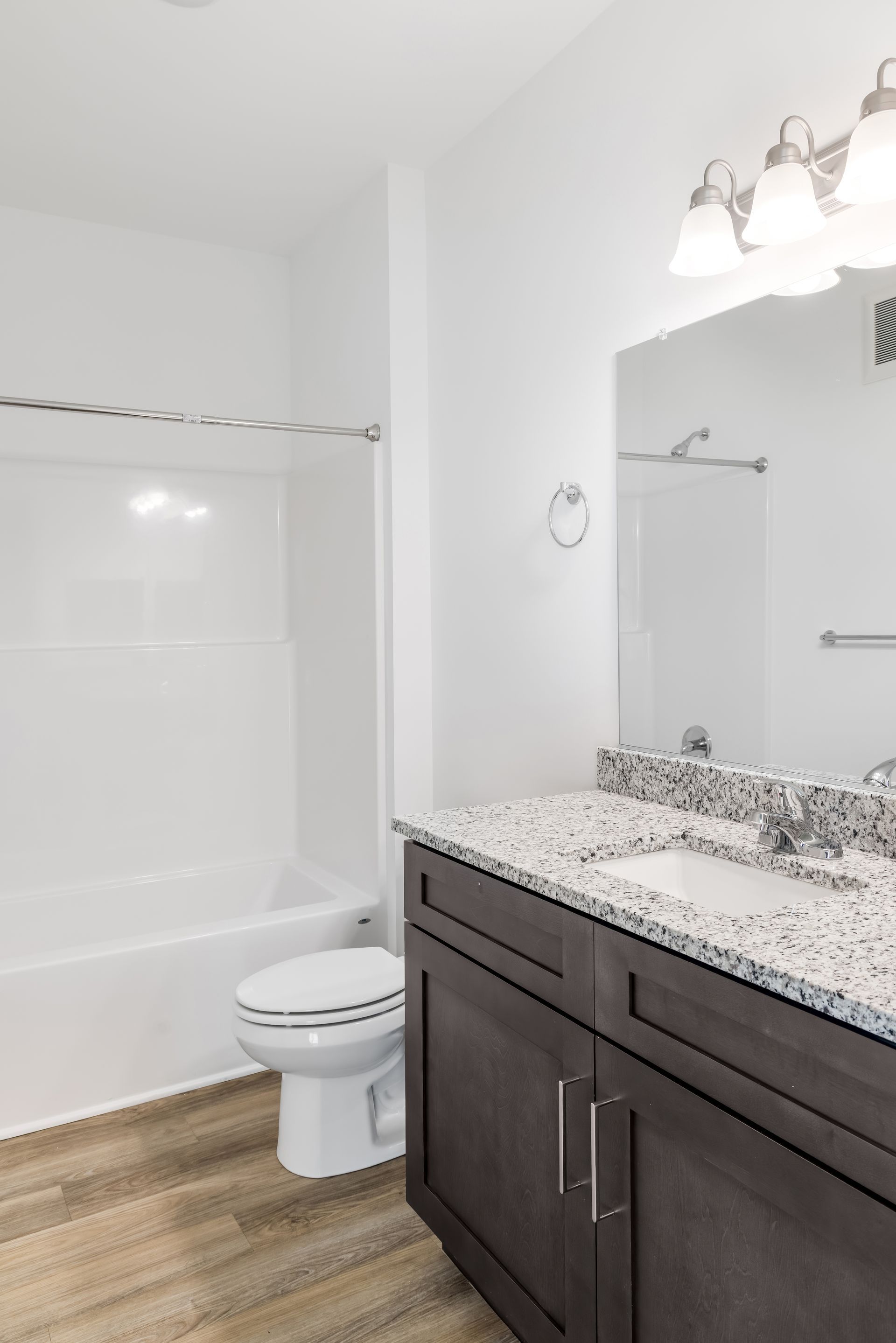 Bathroom with white walls, wood-look floor, dark vanity, granite countertop, and bathtub/shower combo.
