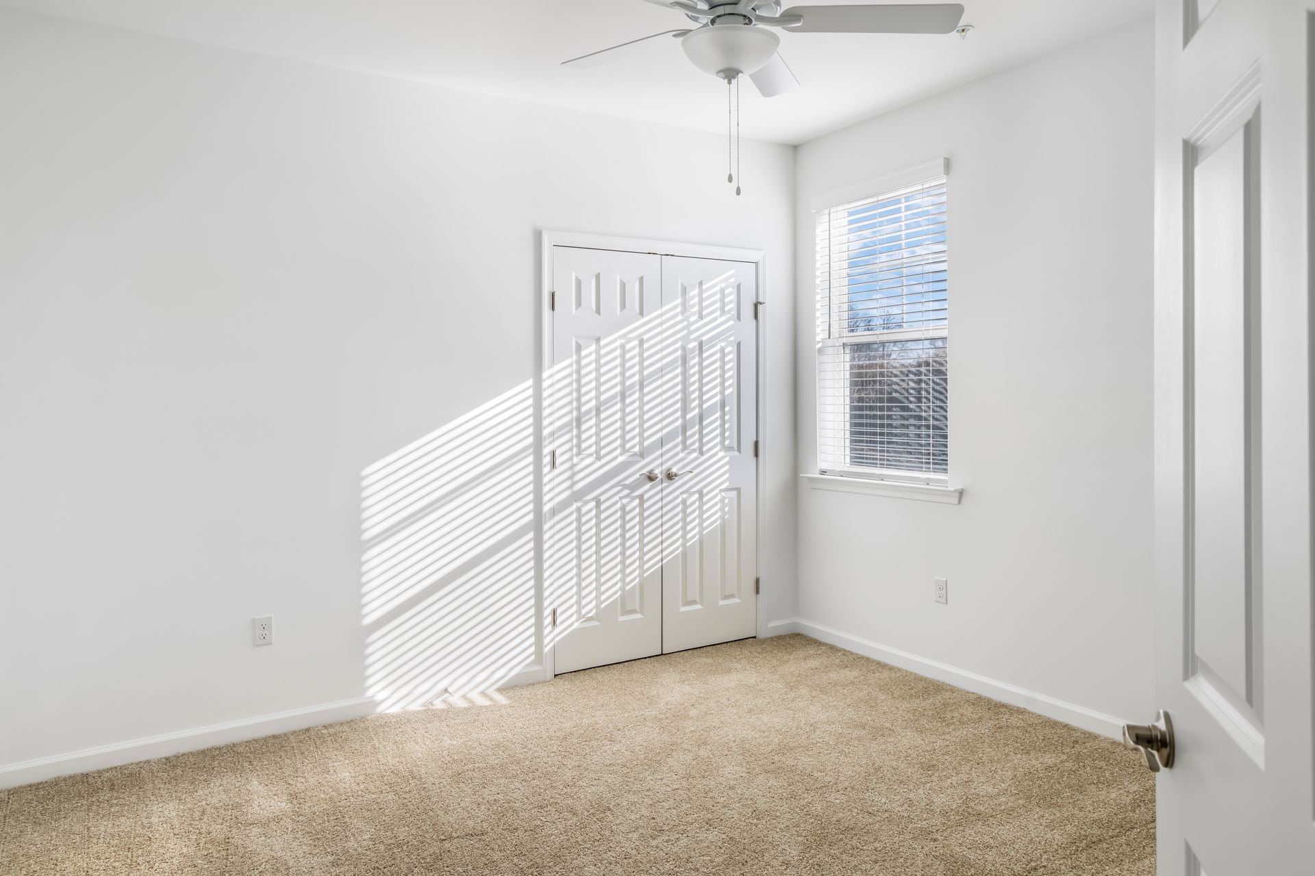 Empty bedroom with closed closet door and window letting in sunlight.