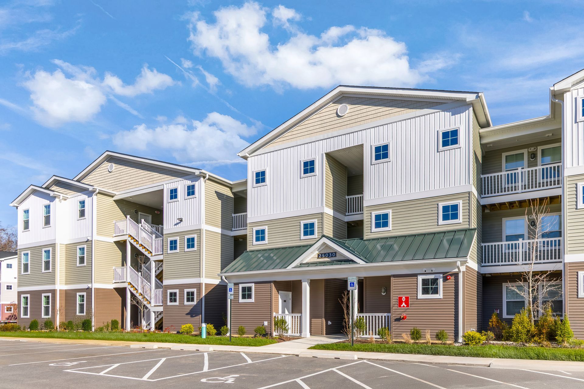 Multi-story apartment buildings with light siding, green roofs, and blue sky.