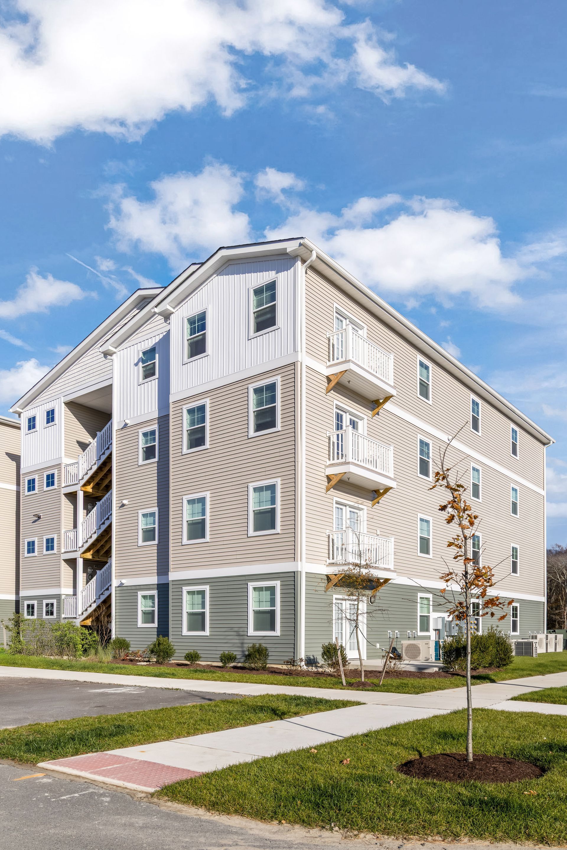 Multi-story apartment building with white and beige siding under a partly cloudy sky.