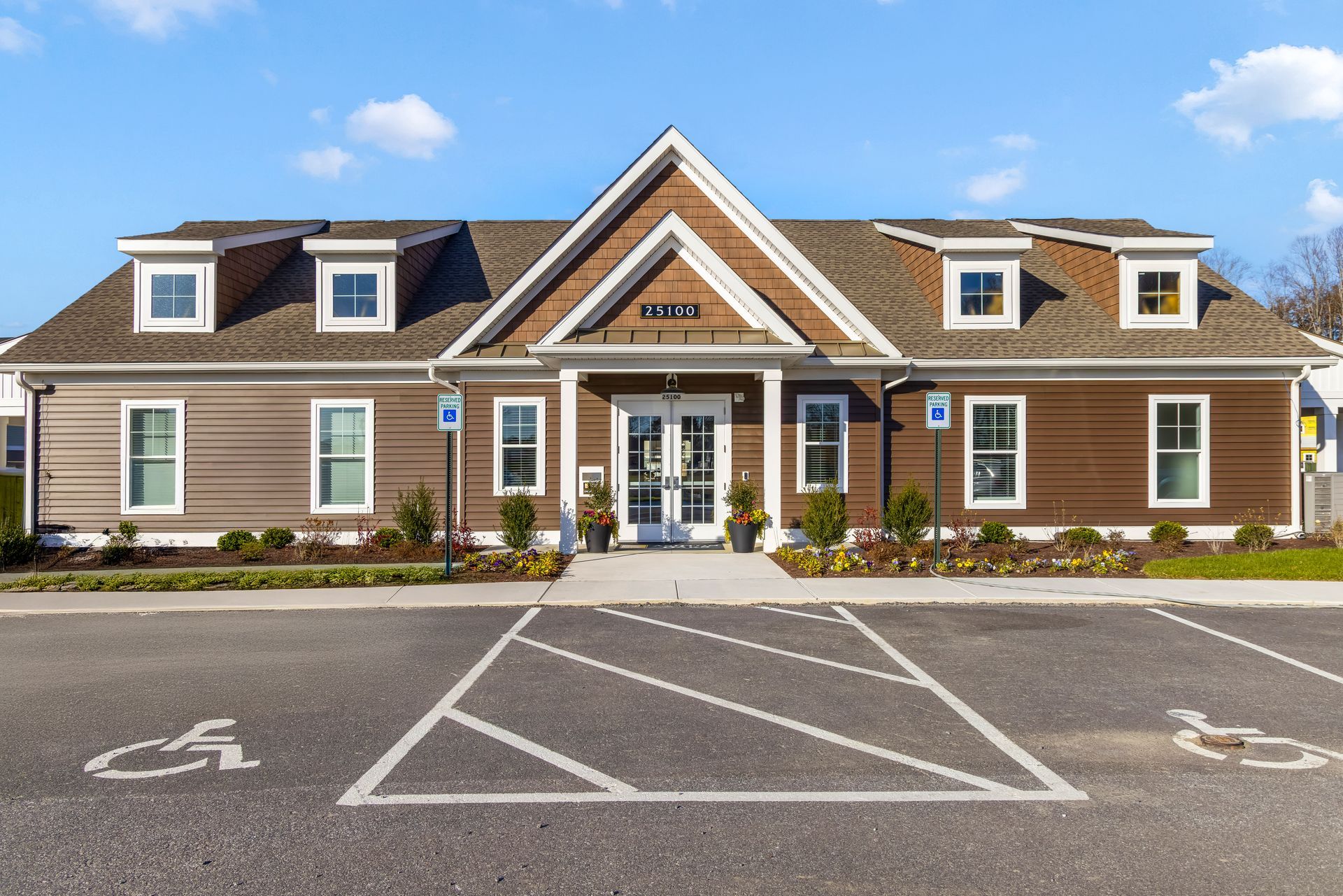 Brown and white building with dormer windows, double doors, and handicap parking spaces.