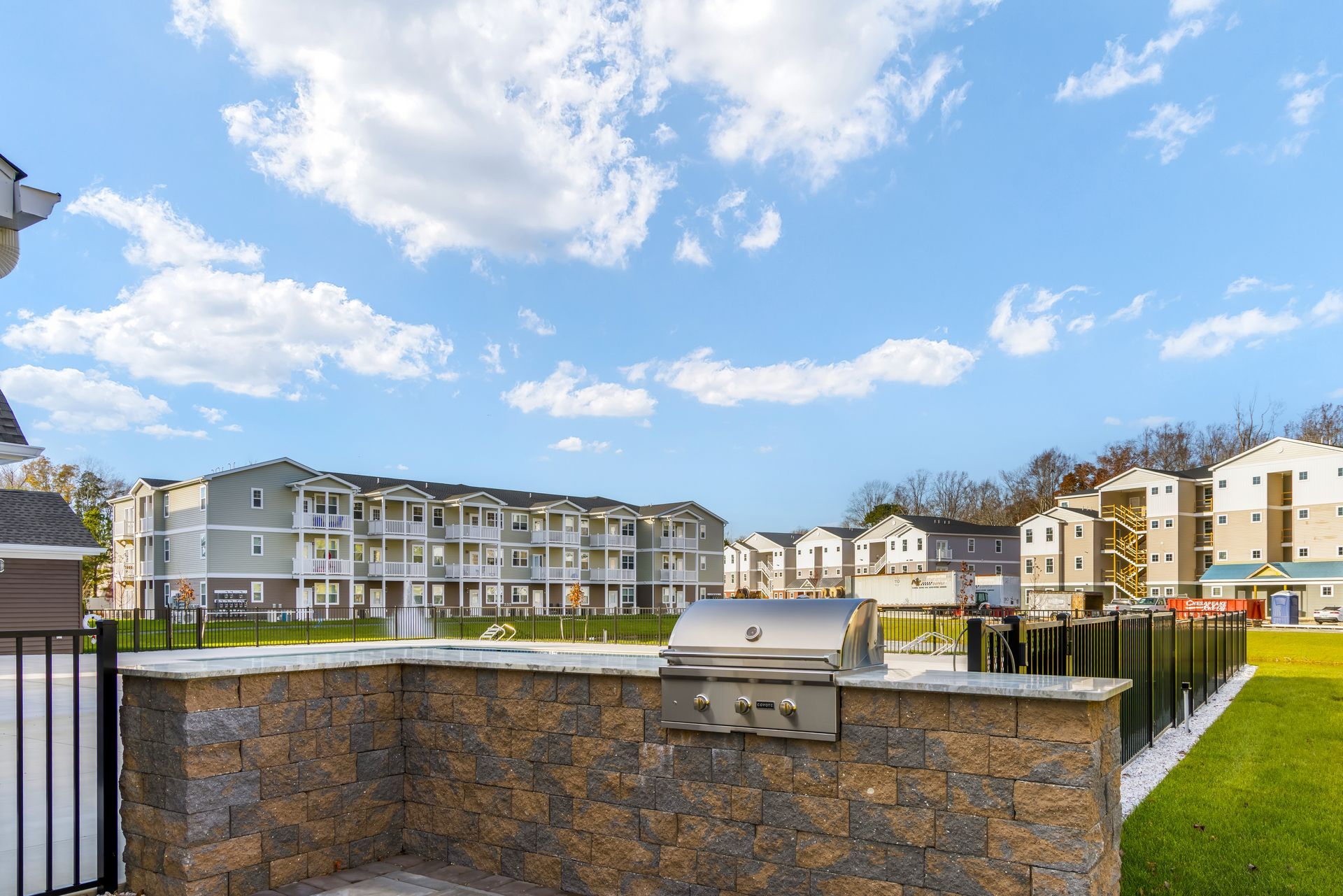 Outdoor barbecue grill built into a stone wall, with apartment buildings and blue sky in the background.