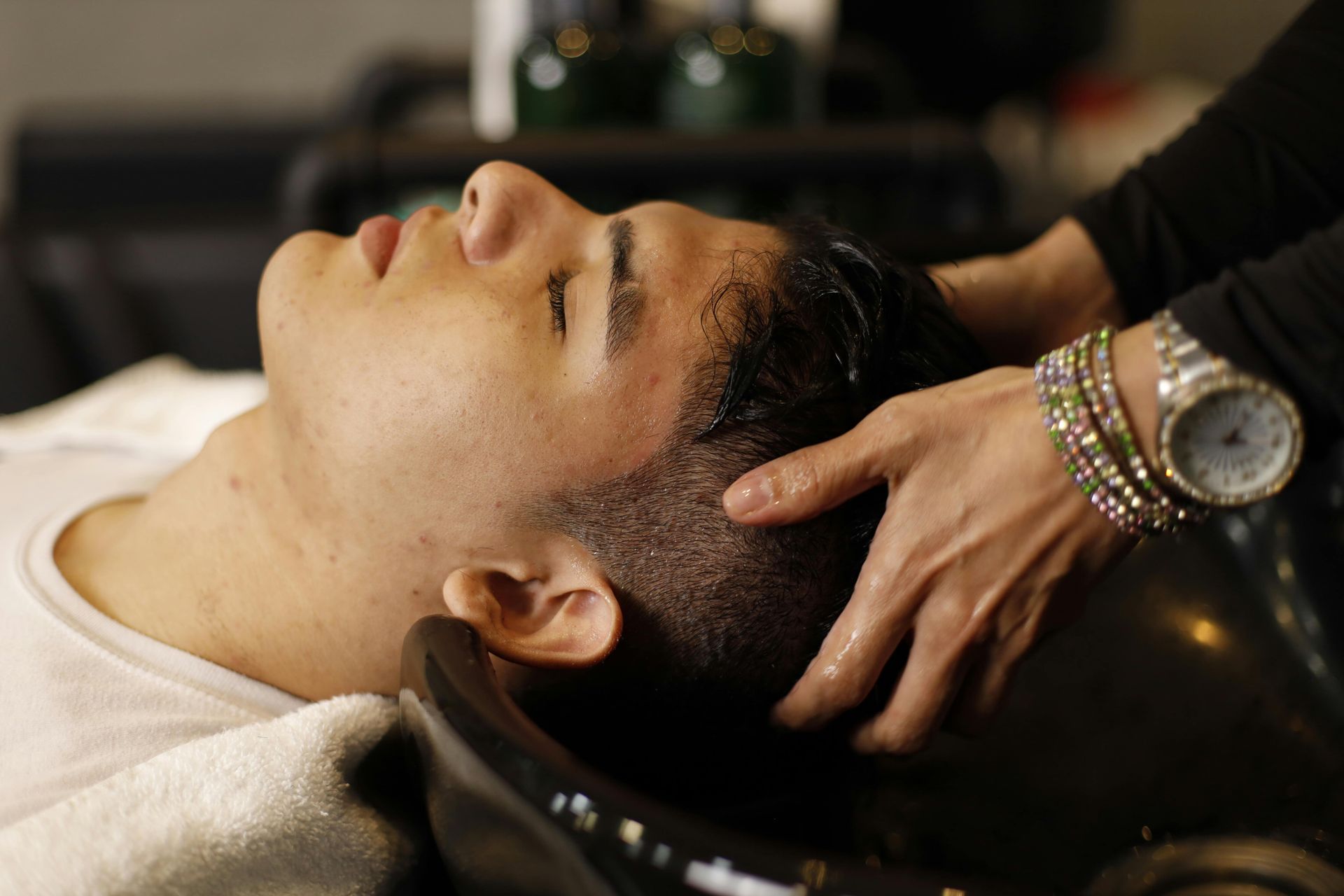 Person having hair washed at a salon. A person's hands are massaging shampoo into the hair over a sink.