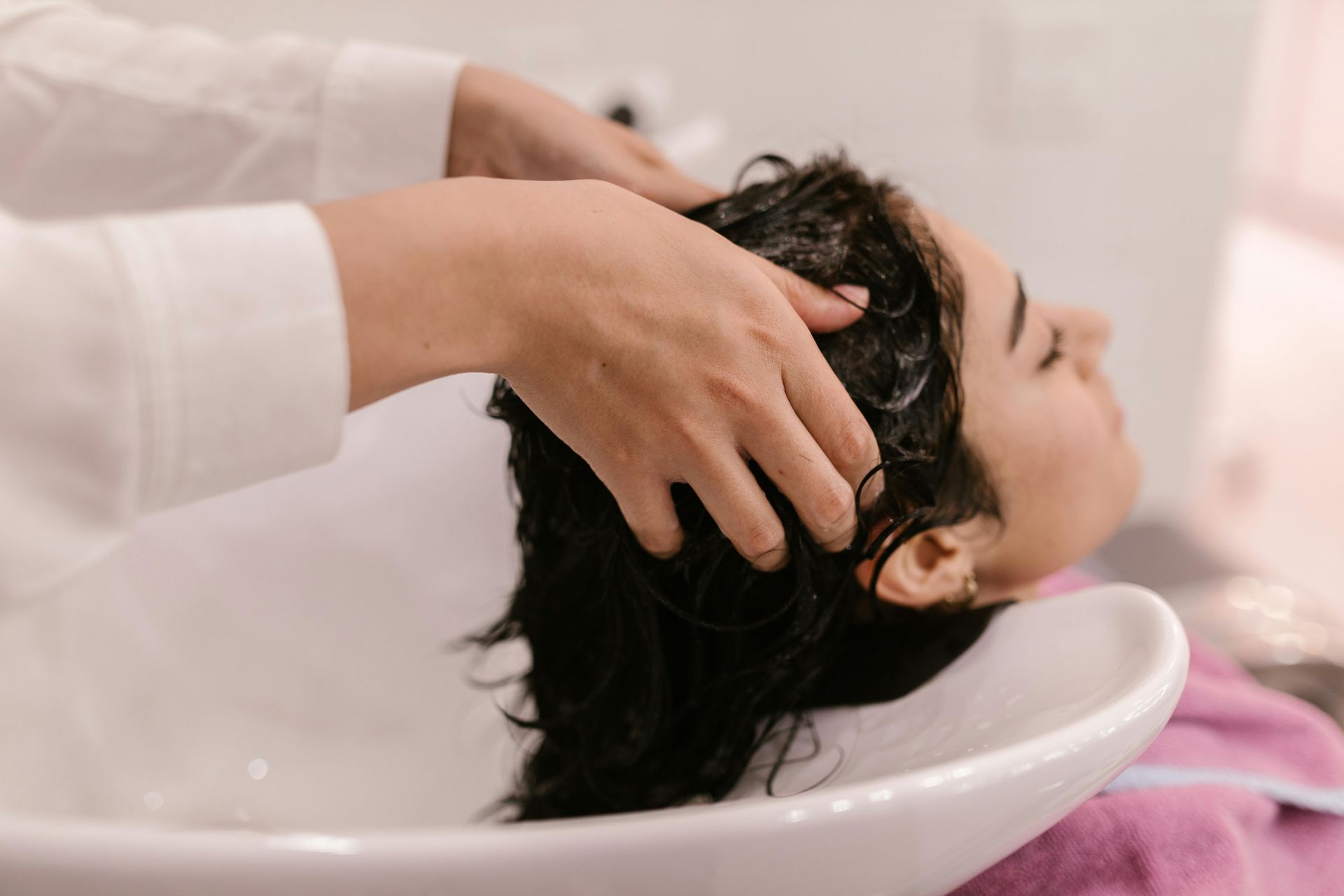Woman having hair washed in a salon sink; hands massaging shampoo.