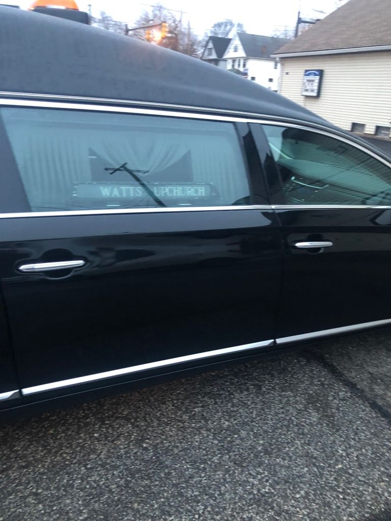 A black hearse parked outdoors, with a partial name visible on the rear side window.