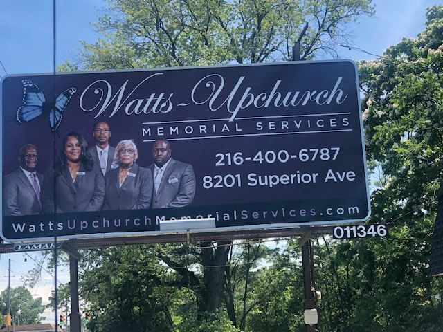 A billboard for Watts-Upchurch Memorial Services featuring five people, a butterfly graphic, phone number, and address.