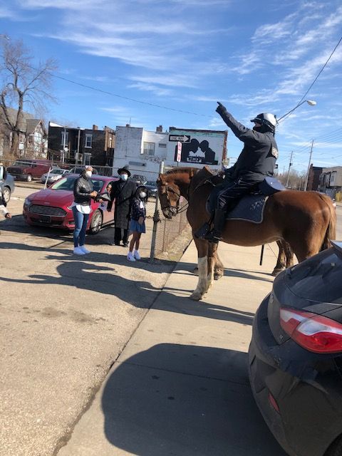 A mounted police officer gestures toward the distance while talking to two individuals on a sunny urban street.