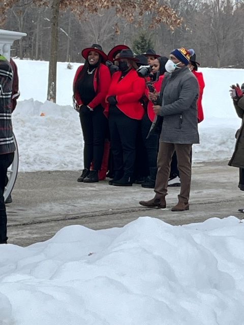 A group of people wearing red and black winter clothing stand on a snowy path, with one person in the foreground.