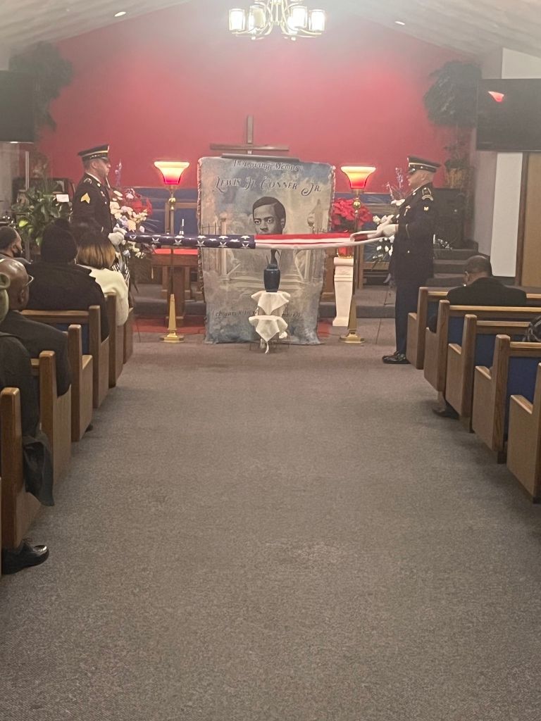 Two service members in uniform stand on either side of a memorial display draped with an American flag inside a church.
