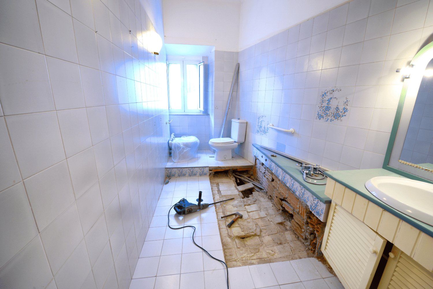 Bathroom renovation in progress; floor partially torn up, walls tiled, toilet and sink present.