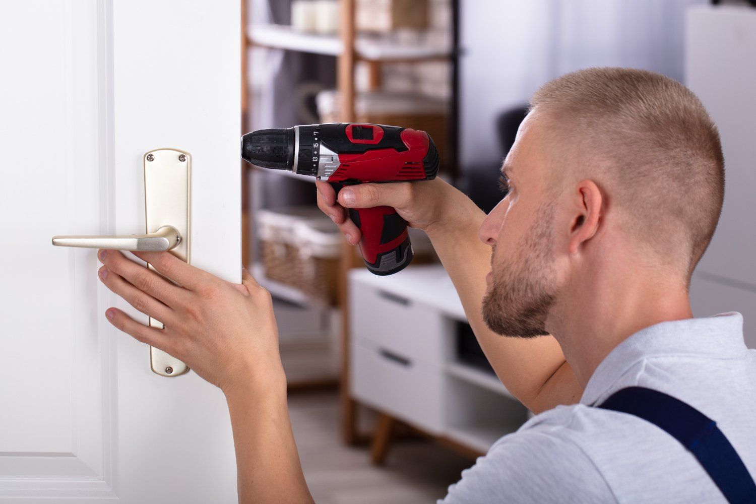 A person is installing a door handle with a drill. They are in a brightly lit room with white furniture.