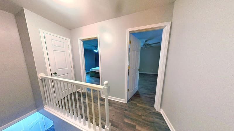Second floor hallway after restoration with fresh drywall, new hardwood-look flooring, and clean white doors