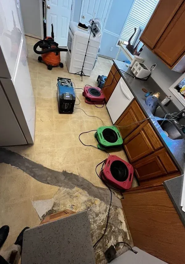 Kitchen floor with water damage. Several fans and a vacuum are drying the damaged floor.