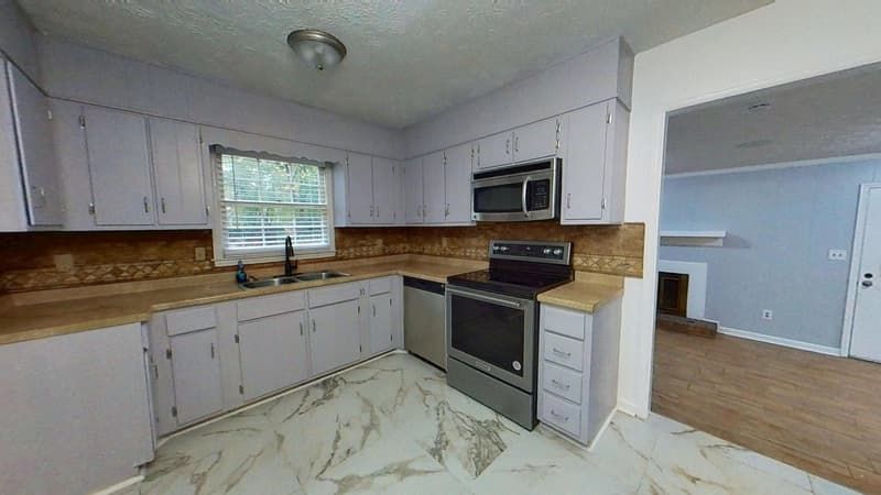 Second kitchen angle after restoration with clean cabinets, tile backsplash, and new flooring