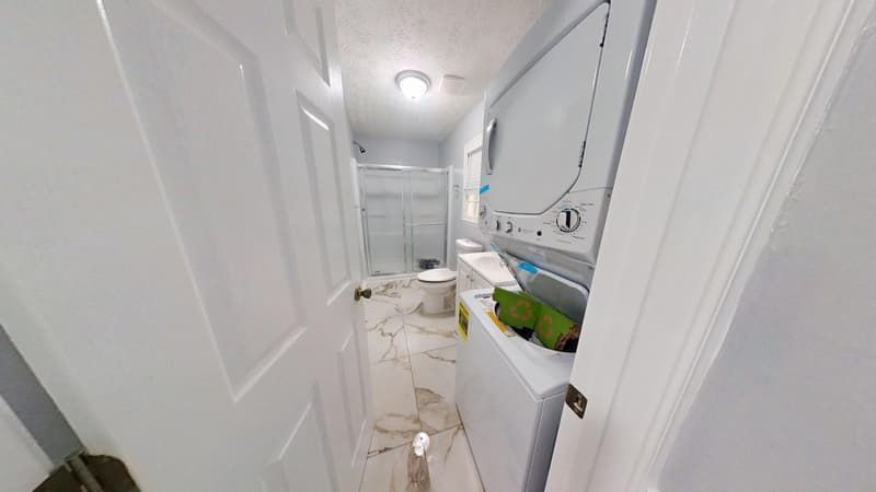 Laundry room after restoration with new marble-look flooring, stacked washer dryer unit, and clean white walls