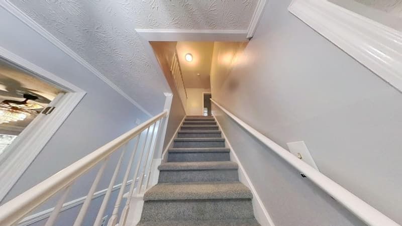 Staircase after restoration with new gray carpet, white painted railings, and clean walls