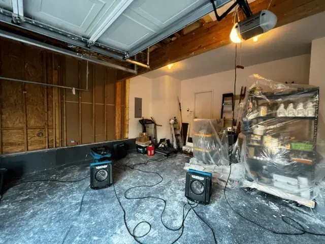 A cluttered garage interior with exposed wood paneling, two speakers wired up, and a covered shelf unit.