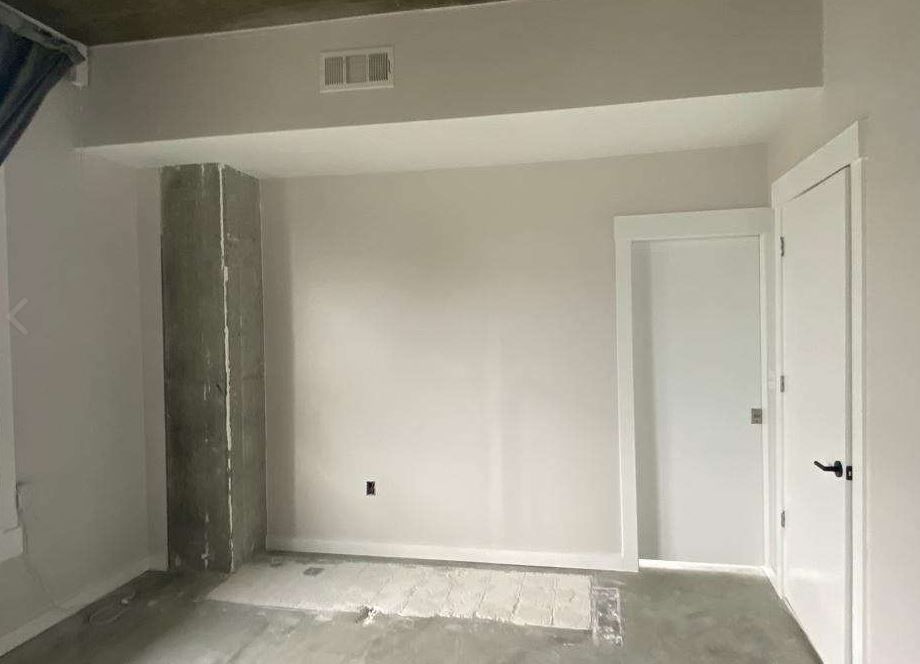 Empty room with a concrete pillar, white walls, door, and grey concrete floor.