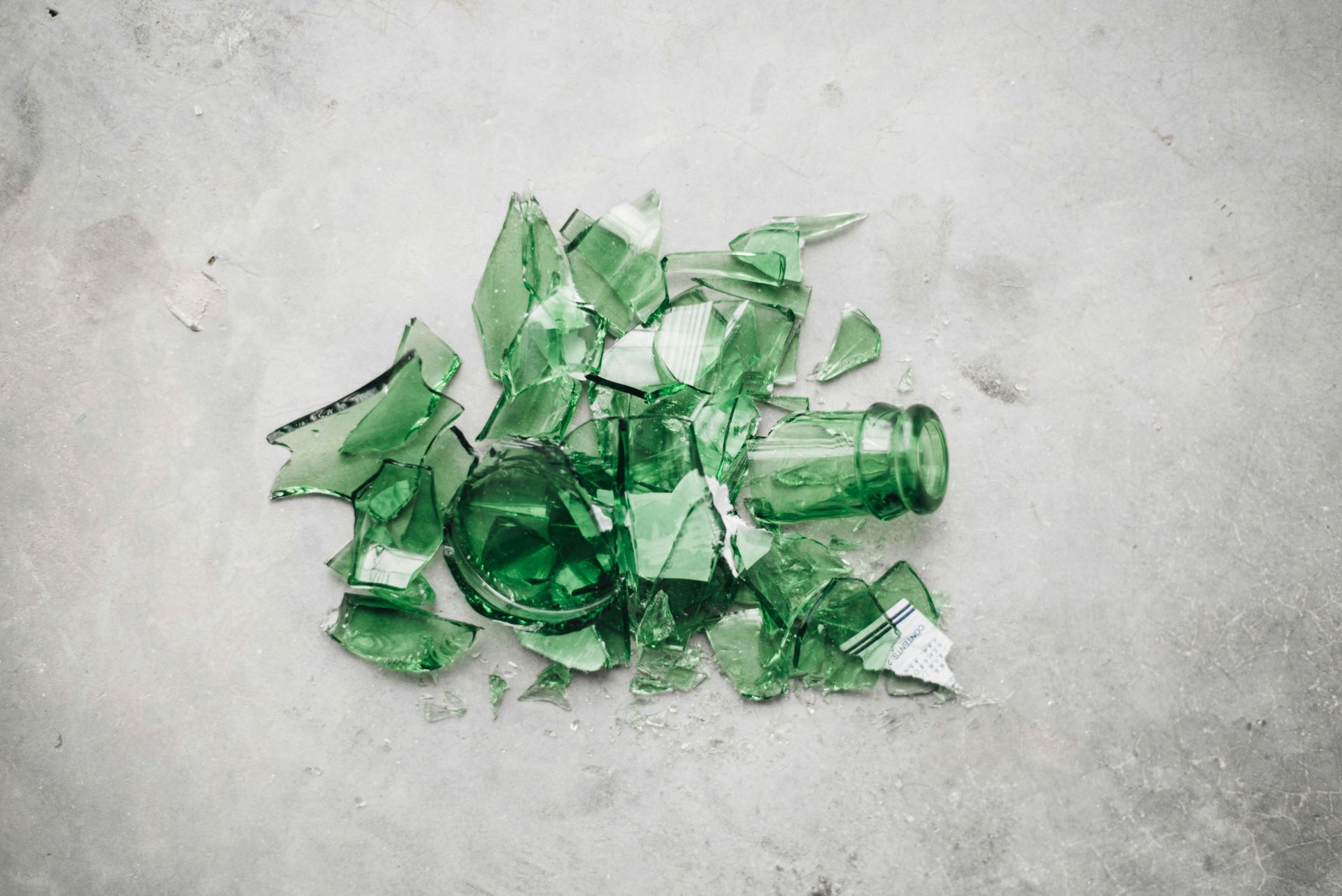 Broken green glass bottles on a concrete floor, ready for safe disposal
