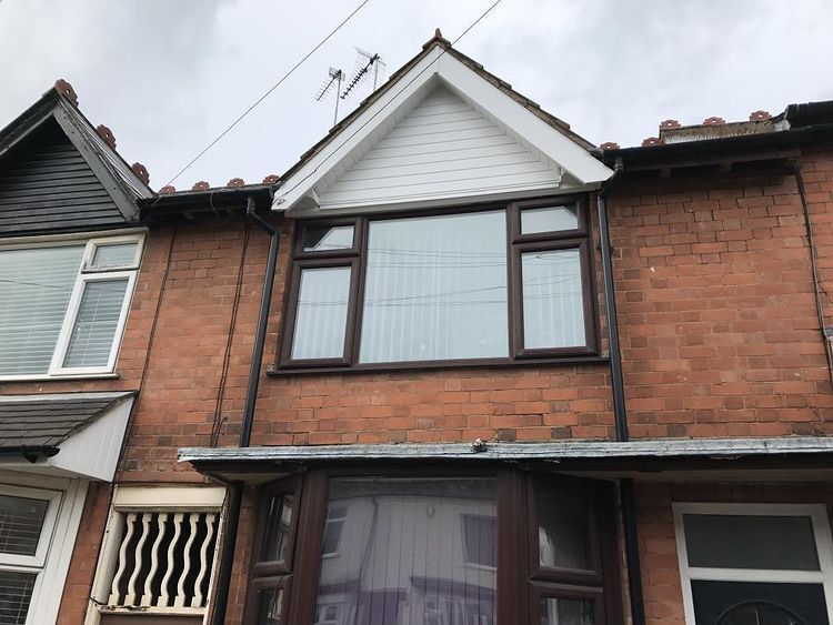 A two-story brick row house exterior with a white-gabled dormer window, brown-framed windows, and a dark front door.