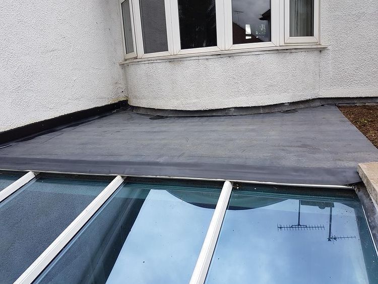 Flat roofing material installed on a section of a building beneath a bay window and a glass roof panel.