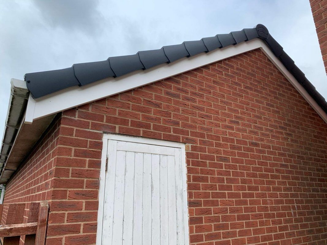 Red brick building with white soffits, dark roof tiles, and a white door.