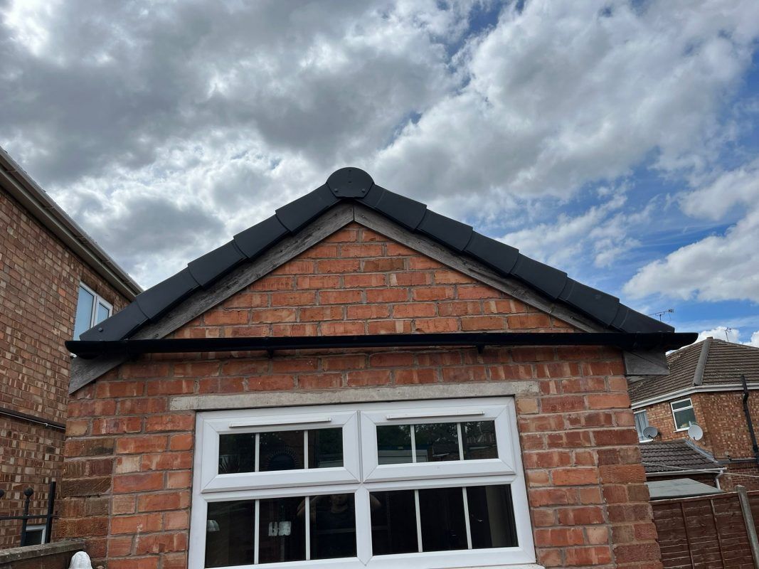 Brick building with black roof tiles and white-framed window against a cloudy sky.