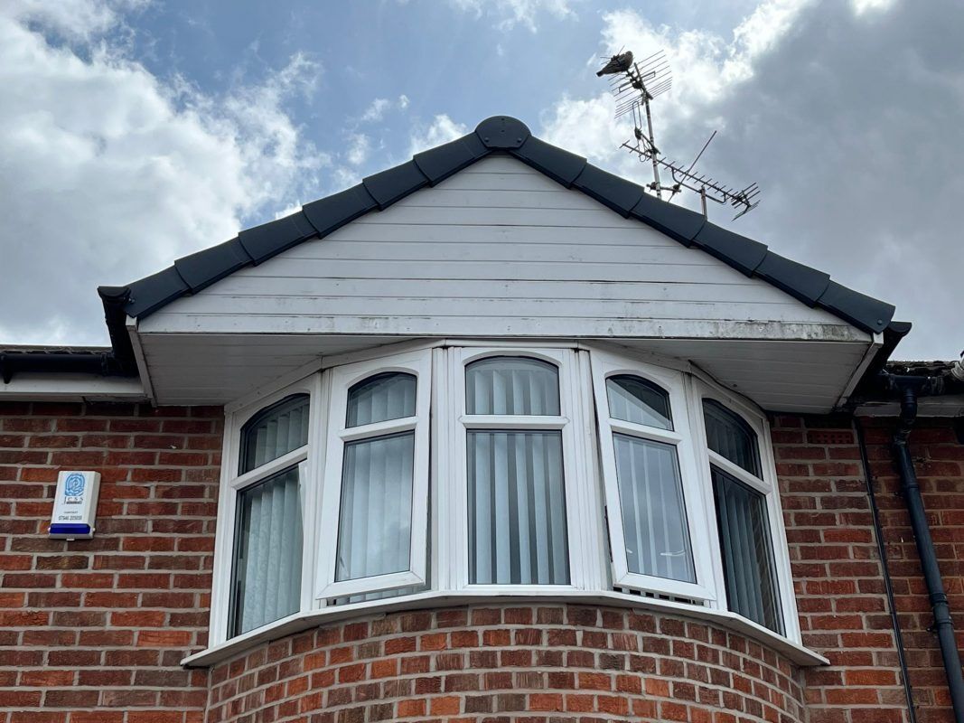 Bay window of a brick house with white soffits, gray roof, and a small bird on an antenna.