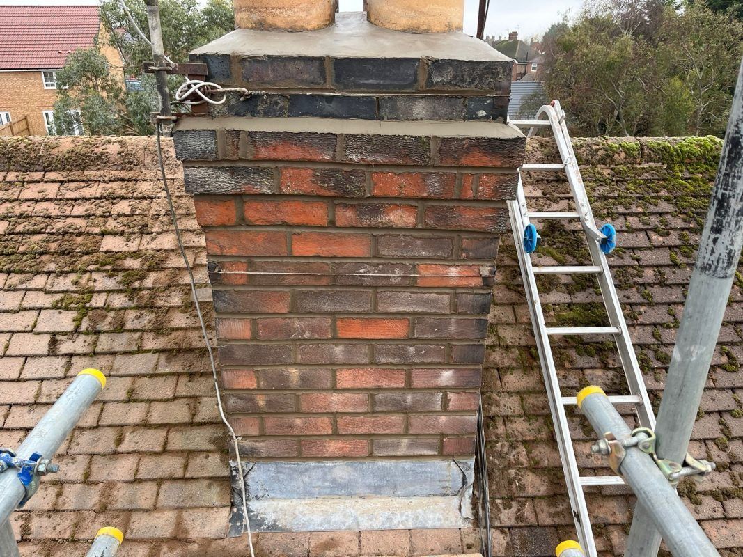 Brick chimney with weathered red bricks, a silver flashing, and a ladder on a rooftop.