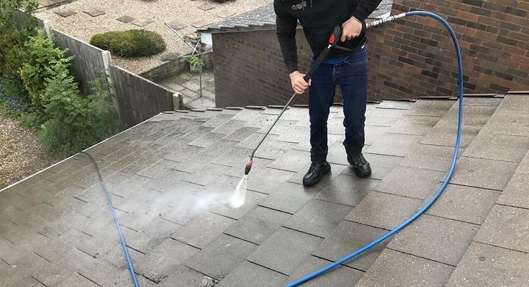 Person on ladder attaching gutters to a roof on a brick house.