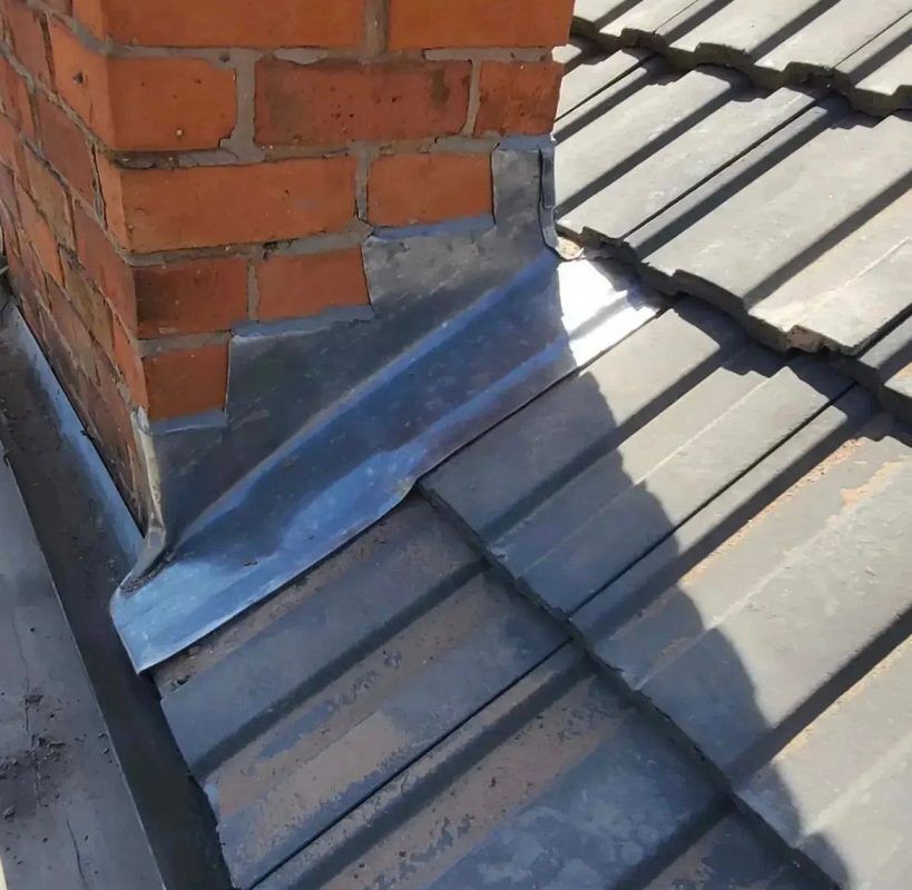 Lead flashing sealed to brick chimney on corrugated roof.