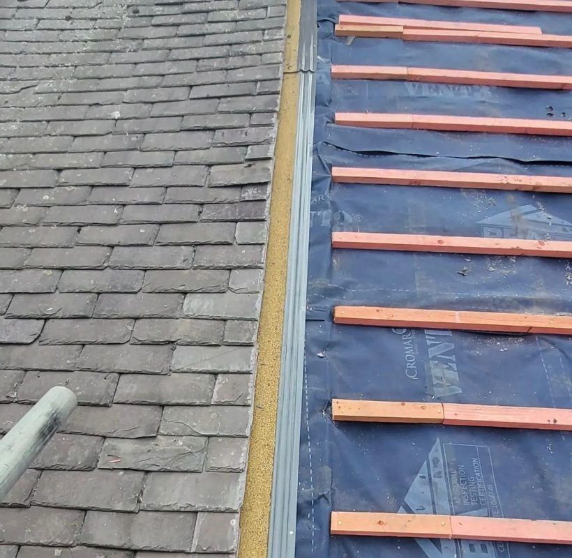 Roof with slate tiles on the left, new underlayment, and wooden supports on the right, separated by a metal flashing.