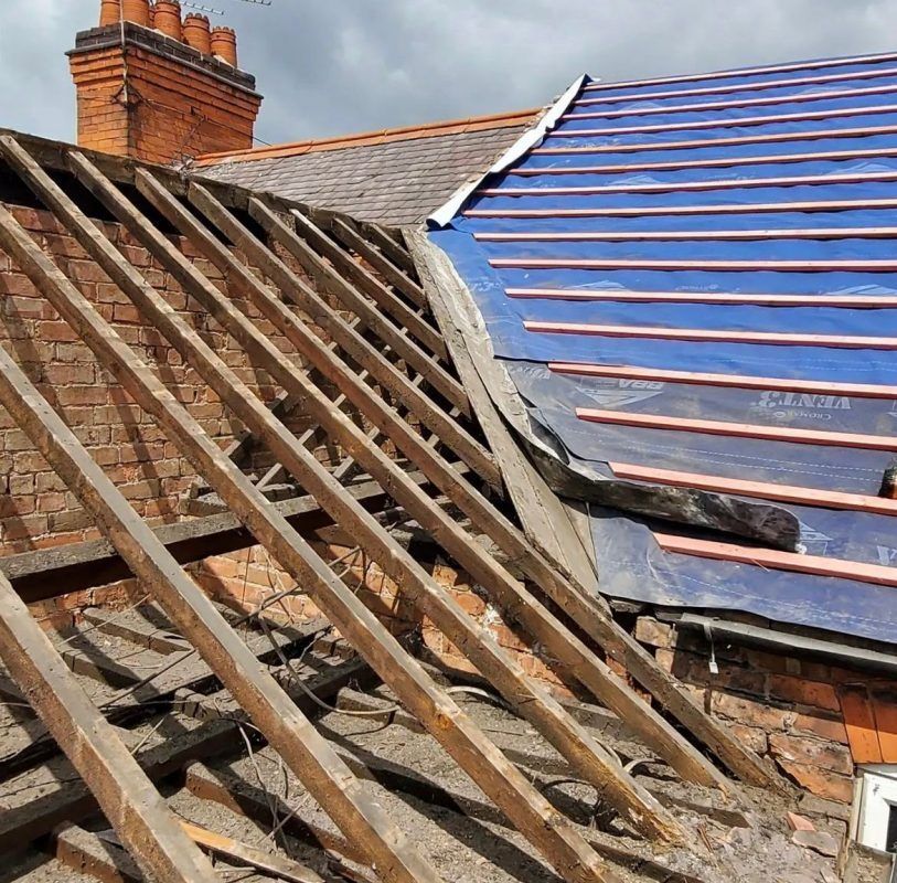 Roof under construction: exposed wooden rafters, blue underlayment, brick chimney, cloudy sky.