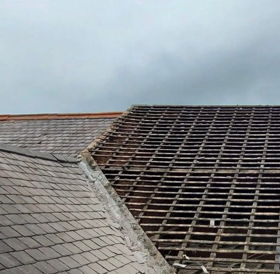 A section of a roof partially stripped of tiles, revealing the wooden lath framework, next to an intact tiled section.