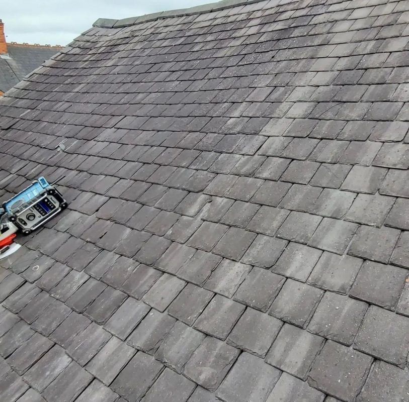 A gray slate-tiled roof with a small, blue electronic leveling tool sitting on the left side.
