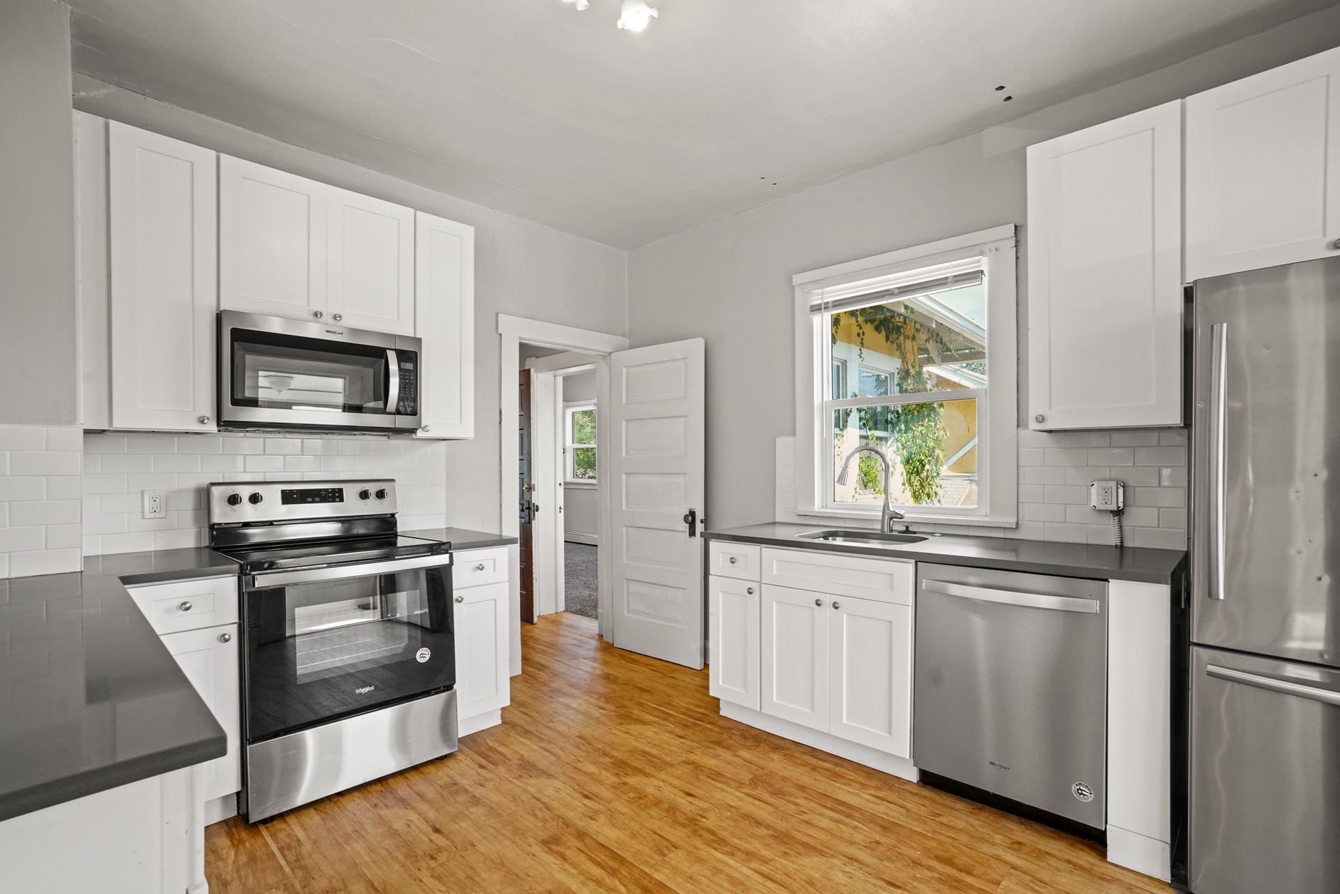 Modern white kitchen with stainless steel appliances, dark countertops, and hardwood floors.