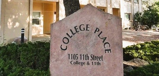 Mountains with a field and three blurred figures walking on a trail under a blue sky.