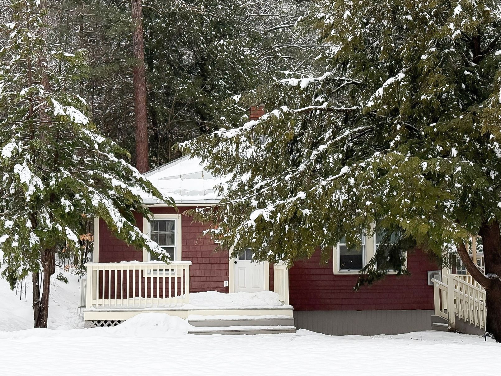 A red house is surrounded by snow covered trees