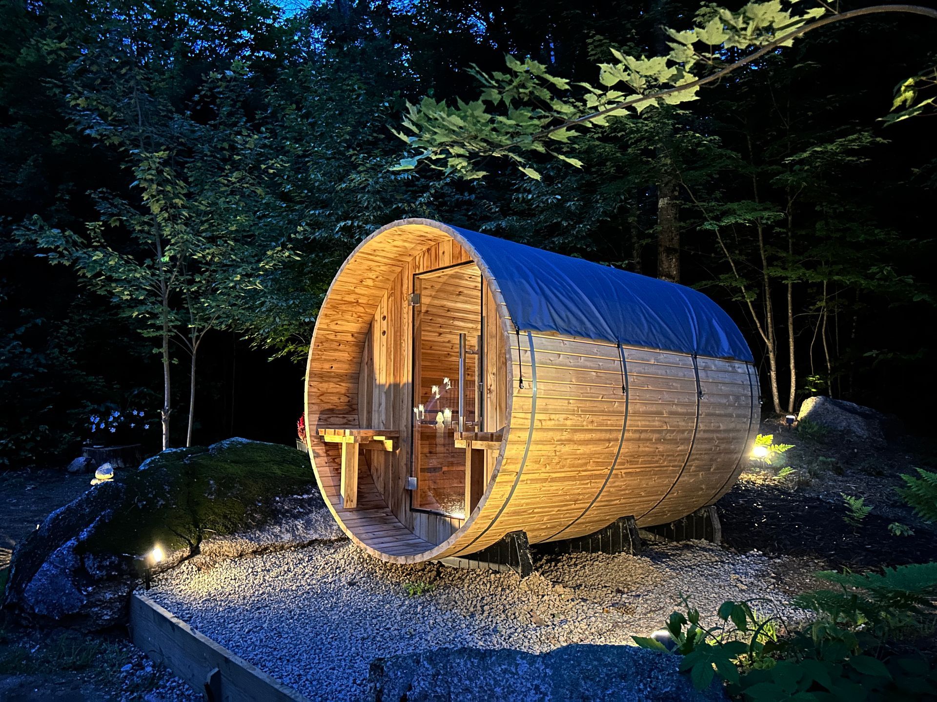 A wooden barrel sauna is sitting in the middle of a forest at night.