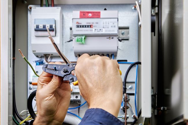 Iemand werkt met een tang aan een elektriciteitskastje.