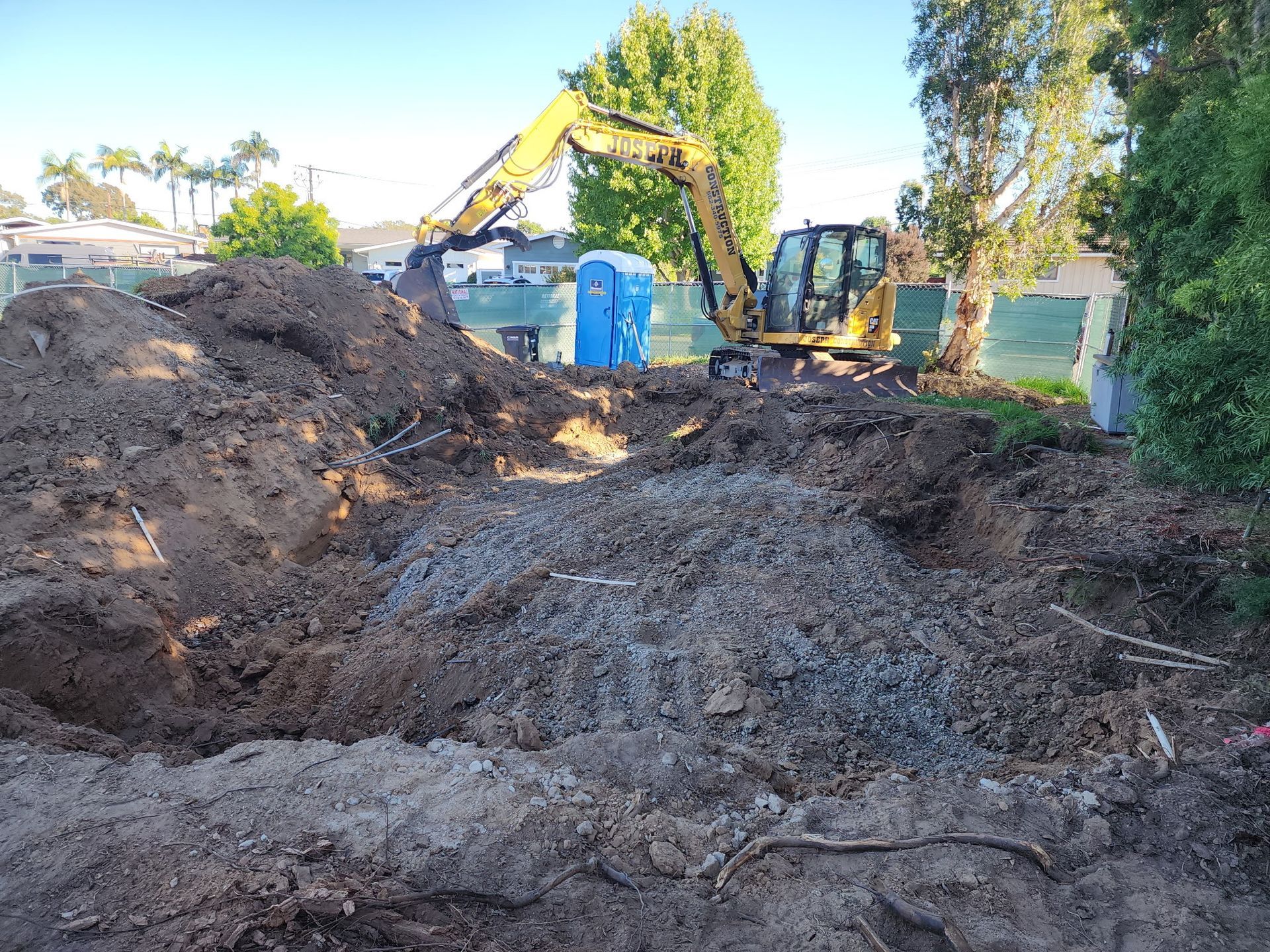 Yellow excavator digging in a dirt lot with a portable toilet.