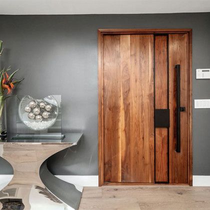 A wooden door with a black handle is in a room with a gray wall.