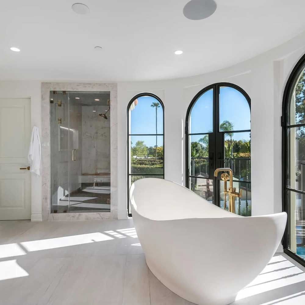 A bathroom with a bathtub , shower , and arched windows.